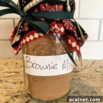 A jar of homemade brownie mix elegantly decorated with a ribbon and fabric top.