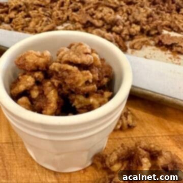 Delicious spiced walnuts in a small jar, next to a baking sheet.