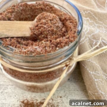 A small jar brimming with homemade taco seasoning, adorned with a spoon and napkin.