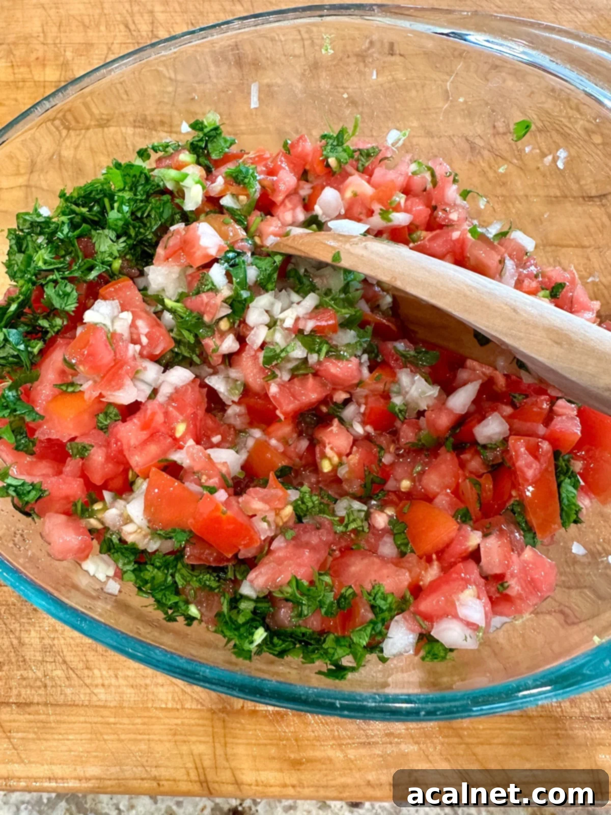 Zesty Jalapeño-Lime Pico de Gallo 10 All the vibrant pico de gallo ingredients, including chopped tomatoes and cilantro, mixed together in a bowl with a wooden spoon.