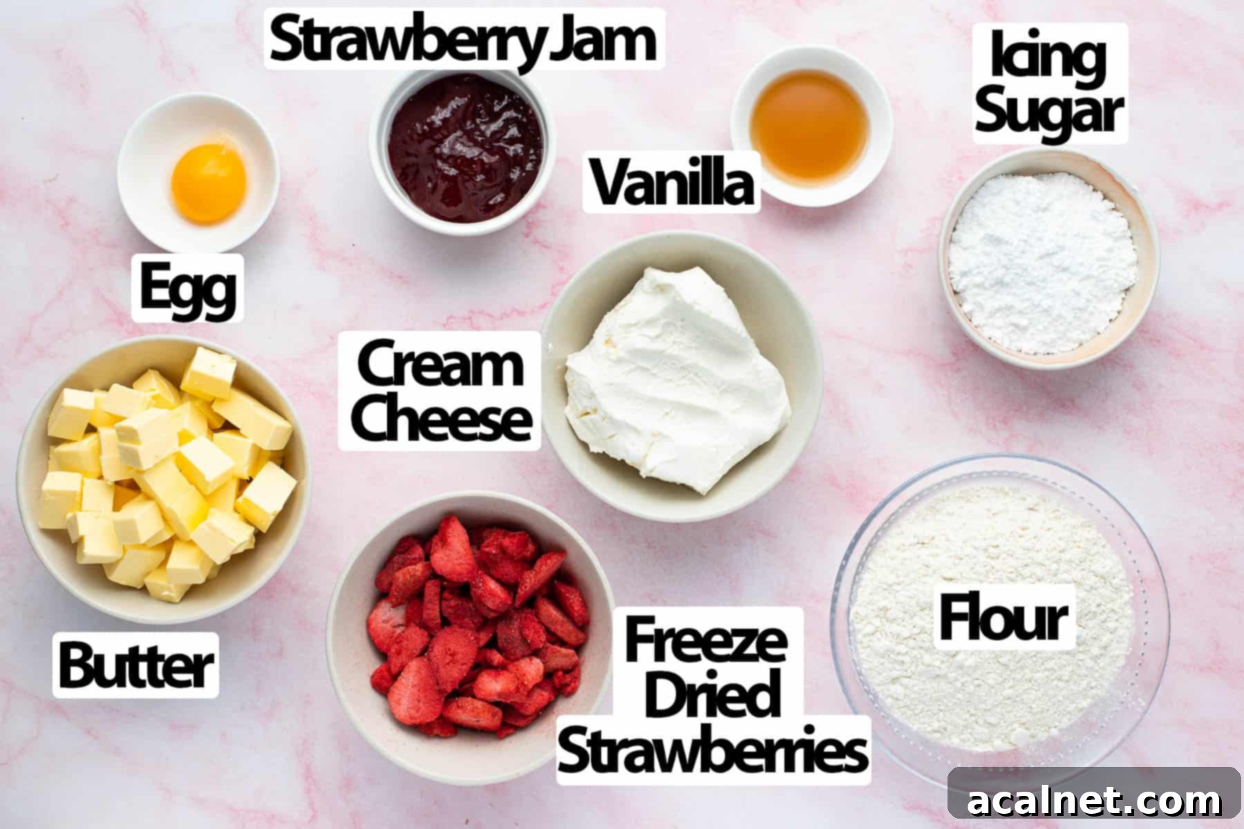 Various baking ingredients including flour, icing sugar, cold butter, eggs, vanilla extract, freeze-dried strawberries, softened cream cheese, and strawberry jam, arranged on a light pink surface.