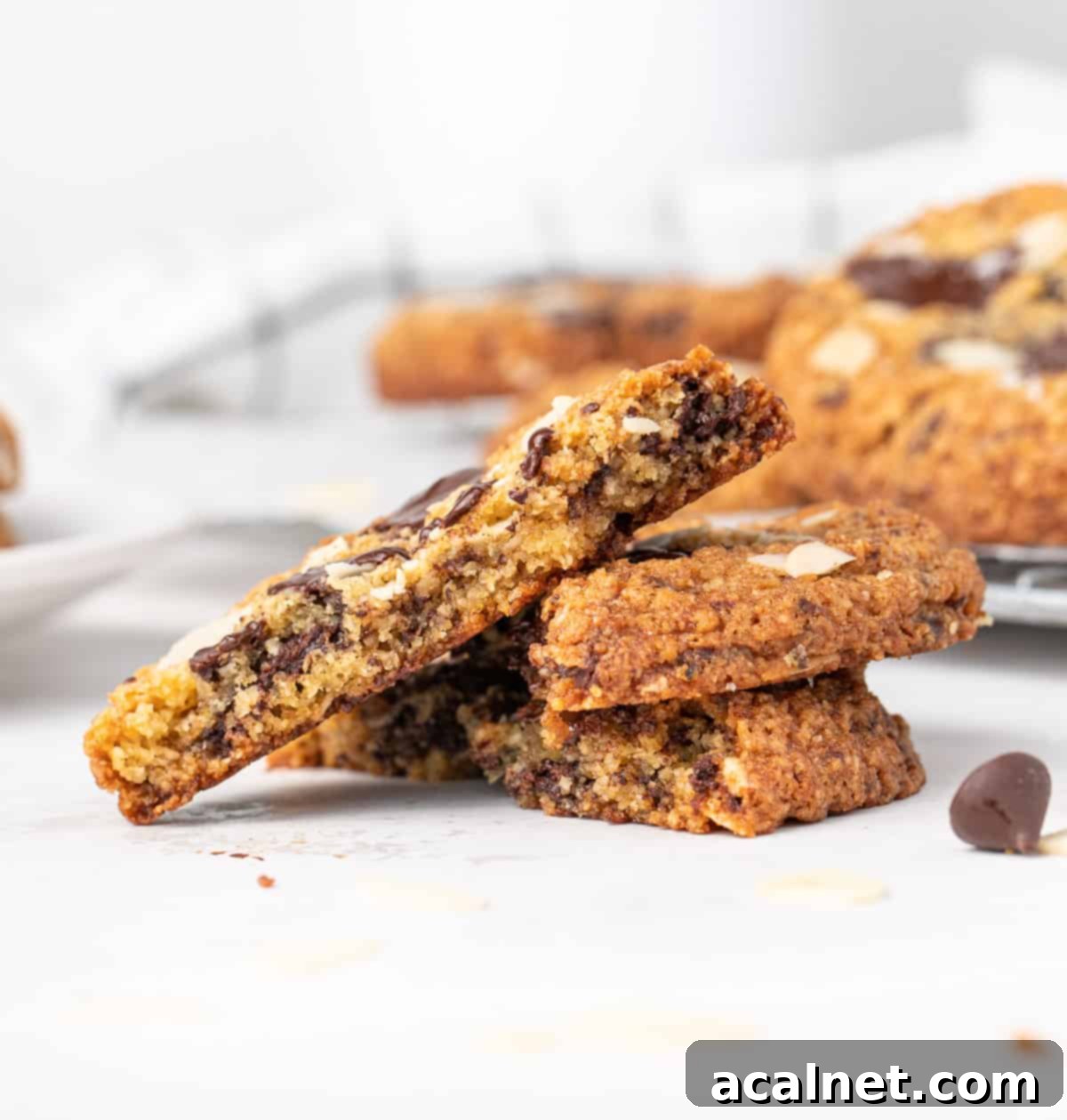 Half a chocolate chip almond cookie balanced on two other halves, showcasing its chewy texture and melted chocolate chunks.