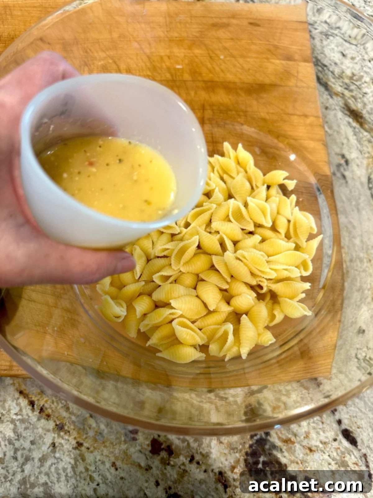 Adding Italian salad dressing to cooked pasta.