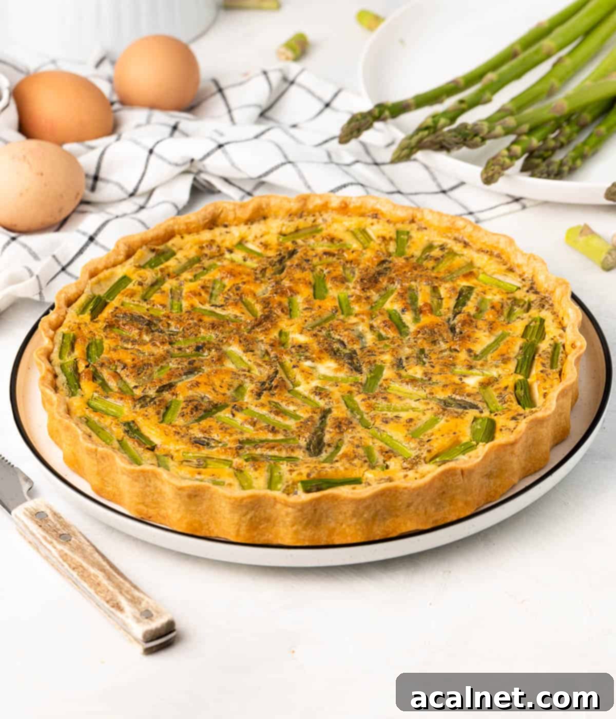 Side view on the quiche placed in a large white plate with ingredients in the background.