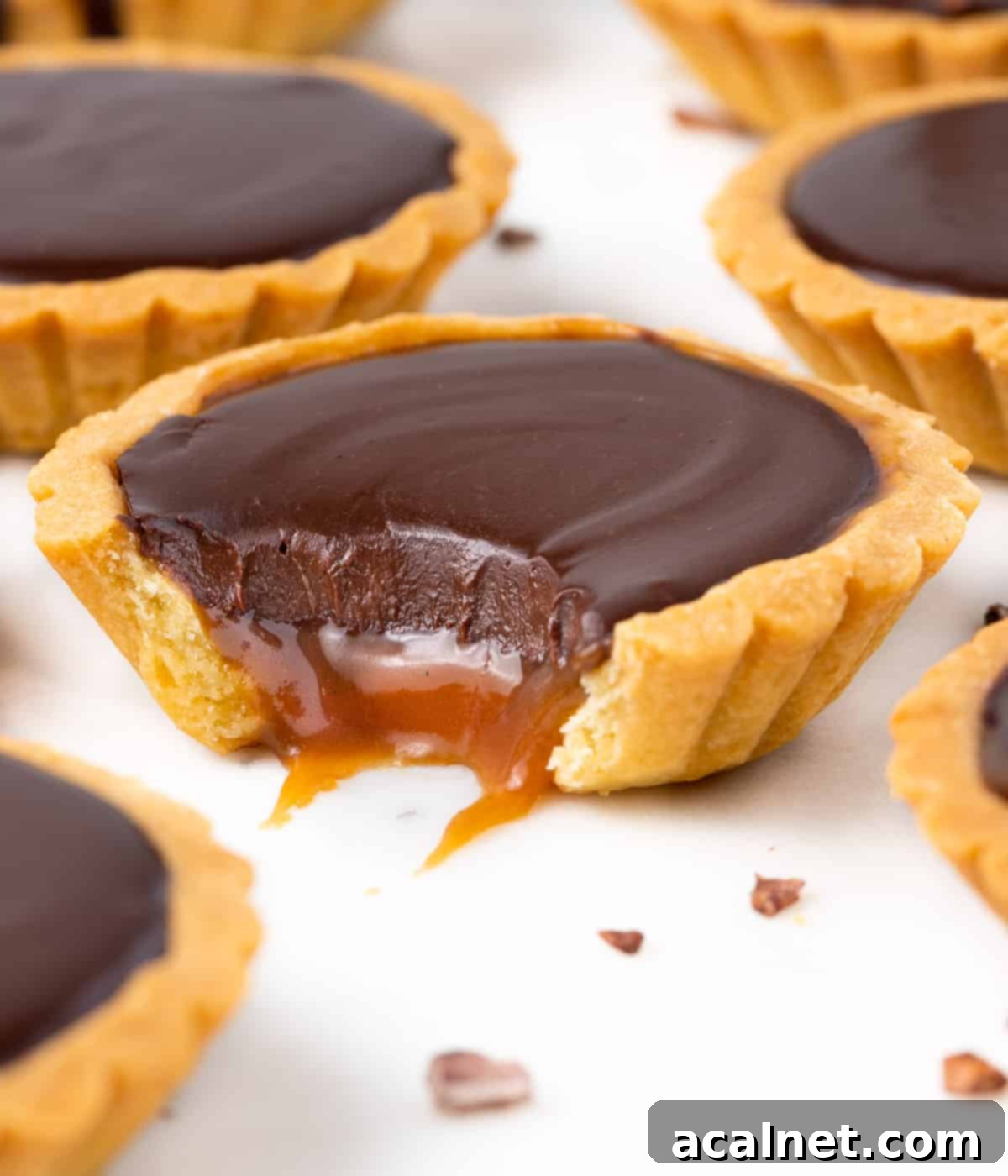 One bite taken off a tartlet with the caramel oozing out.