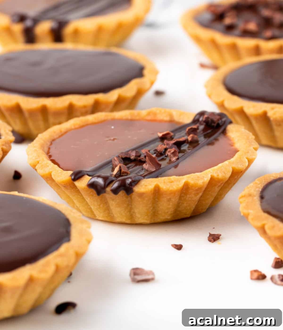 Tarts placed on a white surface with cocoa nibs sprinkled around.