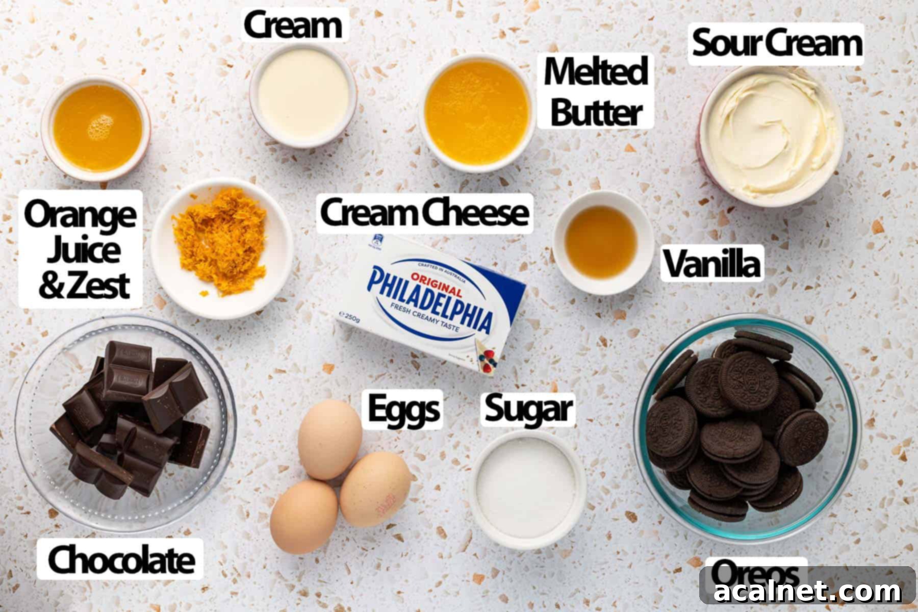 All the necessary ingredients for making a chocolate orange cheesecake are neatly arranged over a stylish terrazzo surface, highlighting fresh oranges, cream cheese, chocolate, and Oreos.