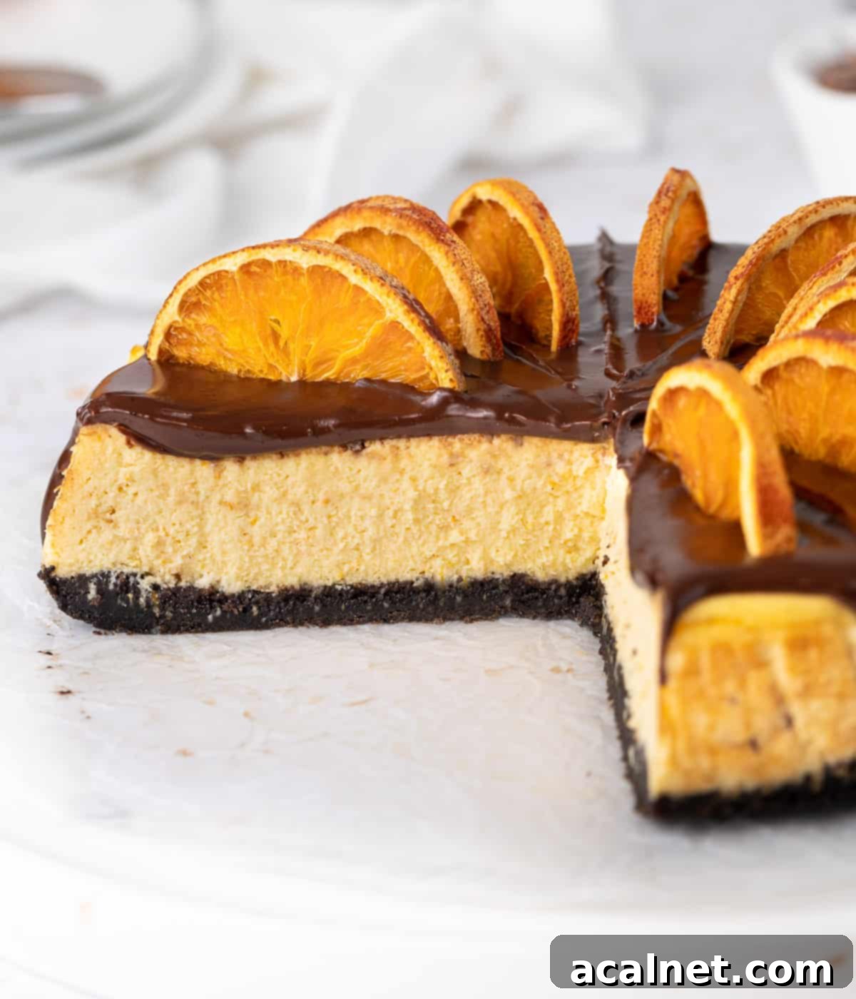 A close-up view of a slice of chocolate orange cheesecake, highlighting the defined layers of the Oreo crust, creamy orange filling, and the rich dark chocolate ganache, with a soft focus on the entire cake in the background.