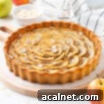 Elegant Apple Frangipane Tart 12 Apple tart on a wooden board surrounded by apples and a stripped tea towel.