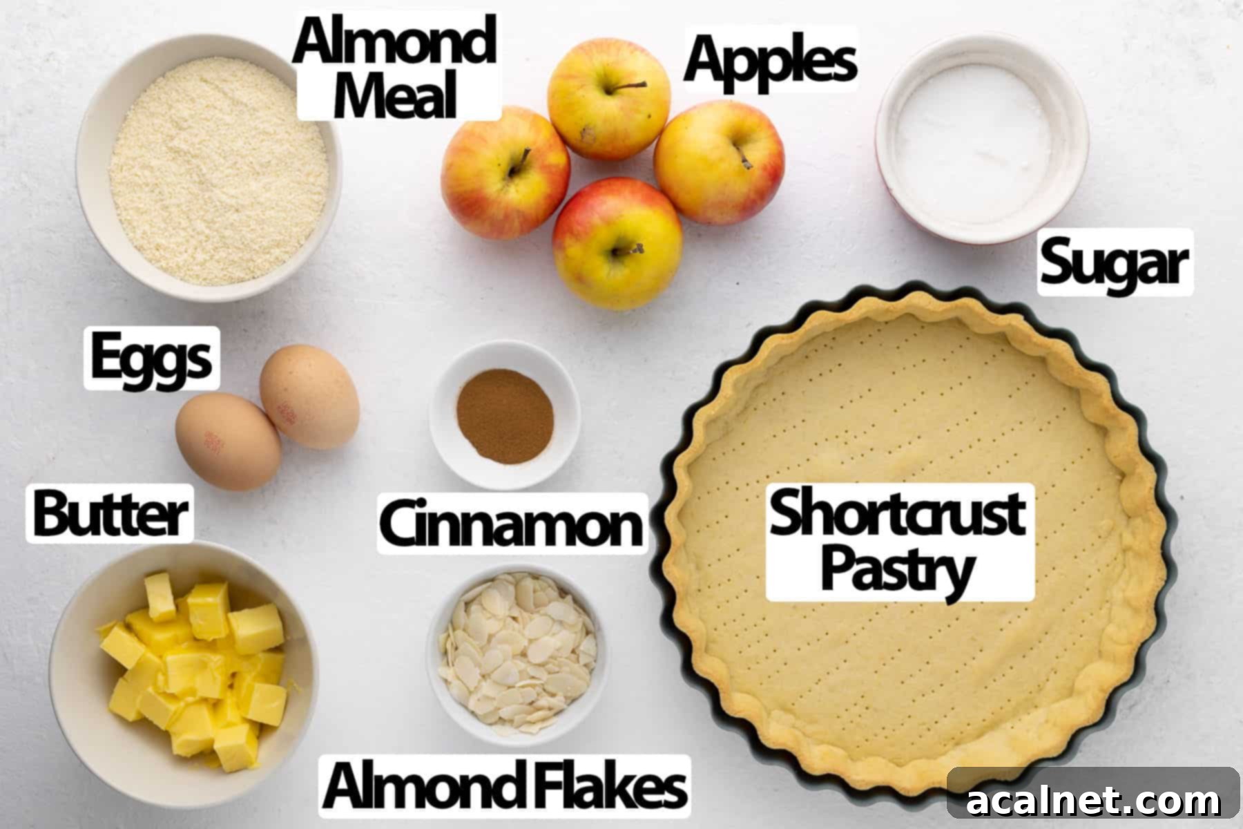 Elegant Apple Frangipane Tart 3 A flat lay photograph showcasing all the ingredients for an Apple Frangipane Tart, including butter, eggs, flour, almond meal, sugar, cinnamon, and fresh apples, laid out on a clean white surface.