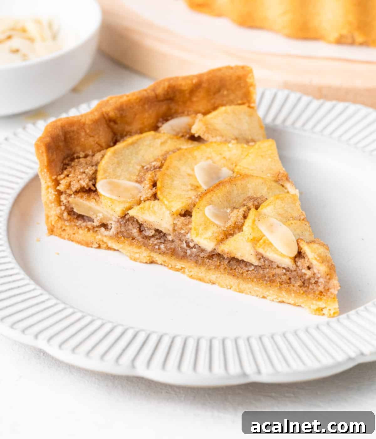Elegant Apple Frangipane Tart 10 A single slice of Apple Frangipane Tart presented on a small, elegant white plate, showcasing its layers of crisp crust, almond filling, and tender apple topping.