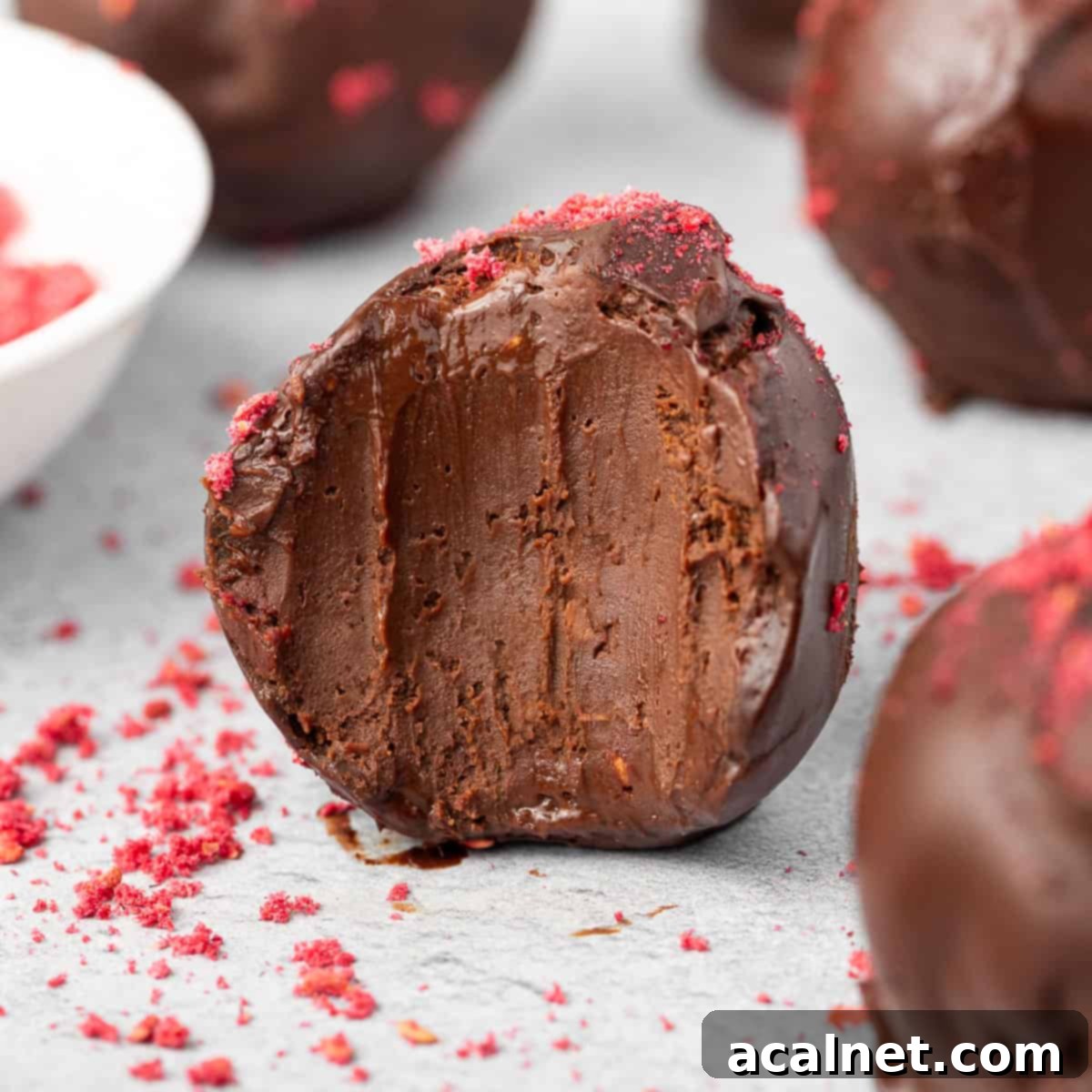 Close up on a truffle with a bite taken off, revealing the creamy raspberry-infused dark chocolate center.