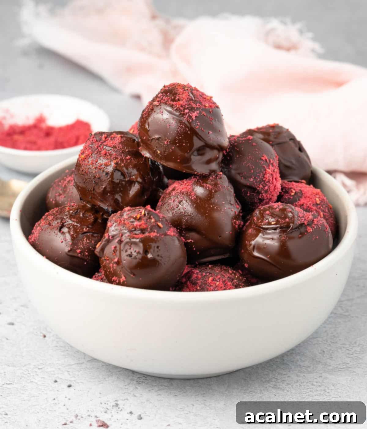Stack of four dark chocolate raspberry truffles in a small white bowl, ready to be enjoyed.