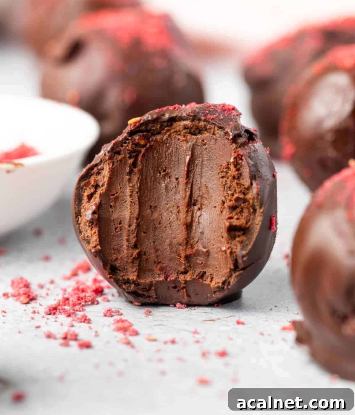 Dark chocolate raspberry truffle with a bite taken off, revealing the vibrant pink raspberry-infused ganache inside.