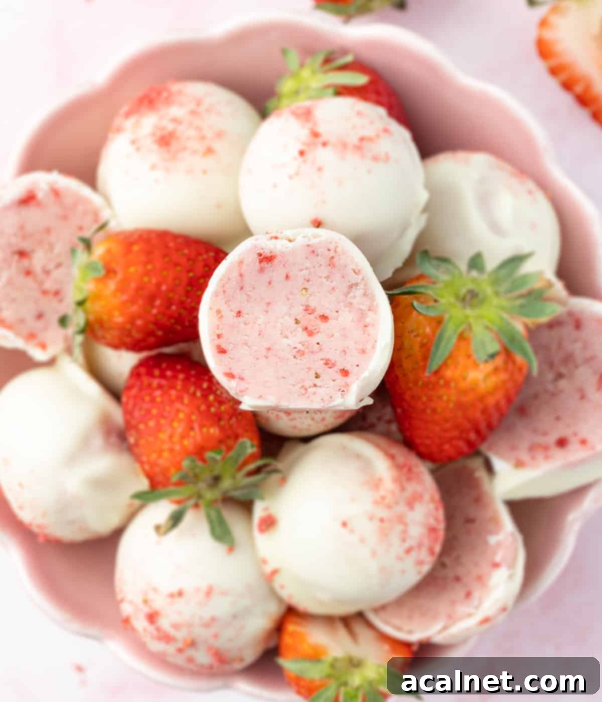 A charming stack of White Chocolate Strawberry Truffles nestled in a small pink bowl, garnished with a few fresh strawberries for a touch of elegance.