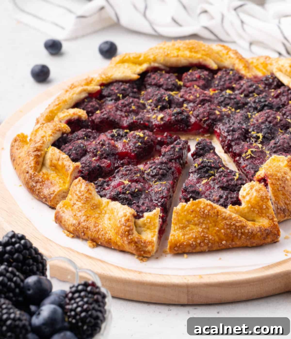 A side view of a baked blackberry galette with three slices already cut and removed, revealing the juicy fruit filling and the flaky crust.