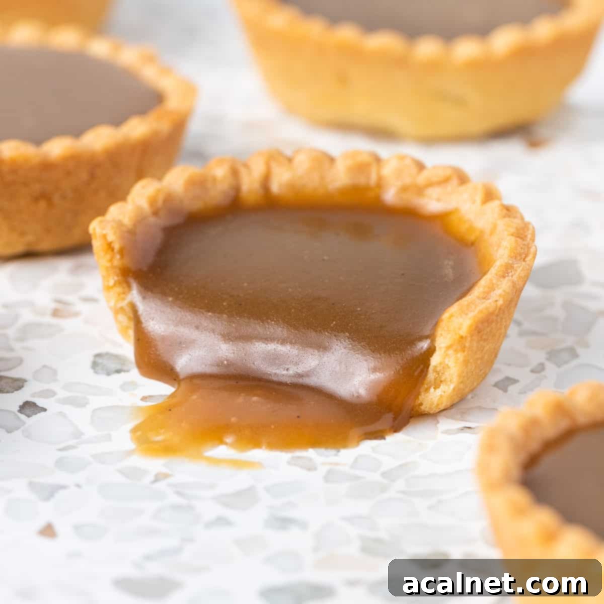 Close up on a tart bite a bite taken off and butterscotch sauce pouring out.