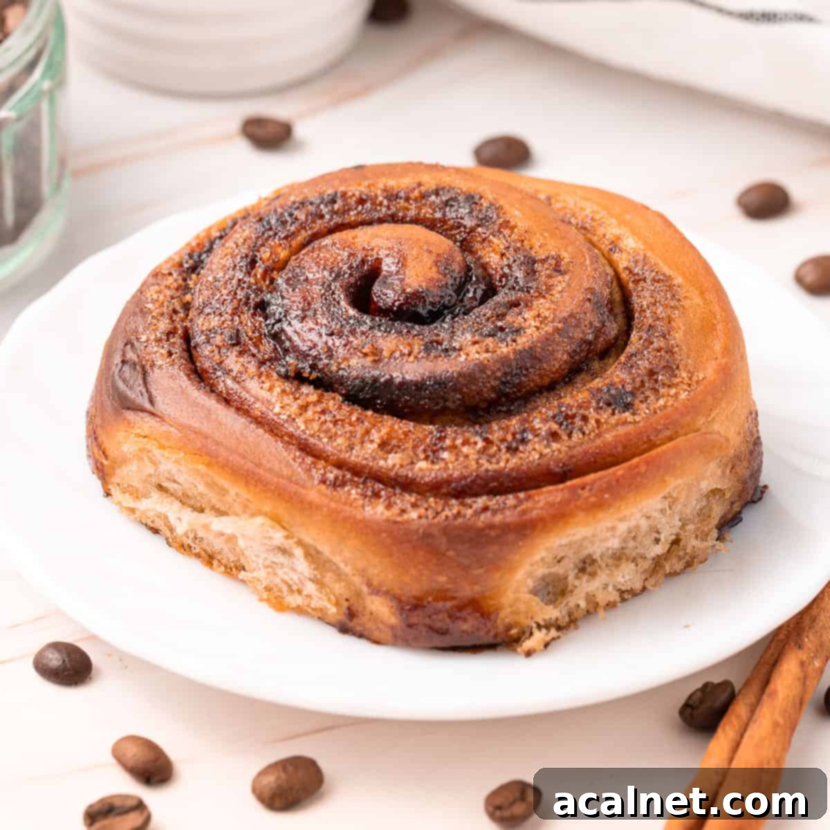 Close up on a roll over a small white plate surrounded by coffee beans, invitingly frosted.