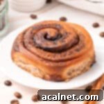 Close up on a roll over a small white plate surrounded by coffee beans