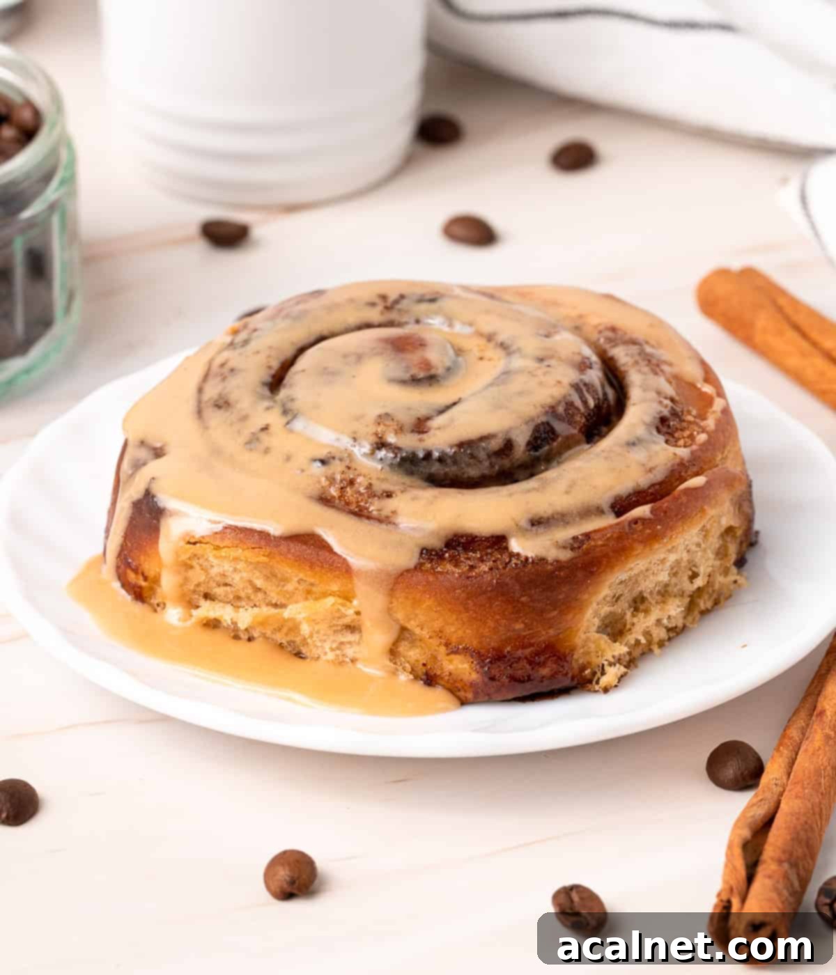 A single coffee cinnamon roll covered in espresso icing, elegantly placed on a small white plate.