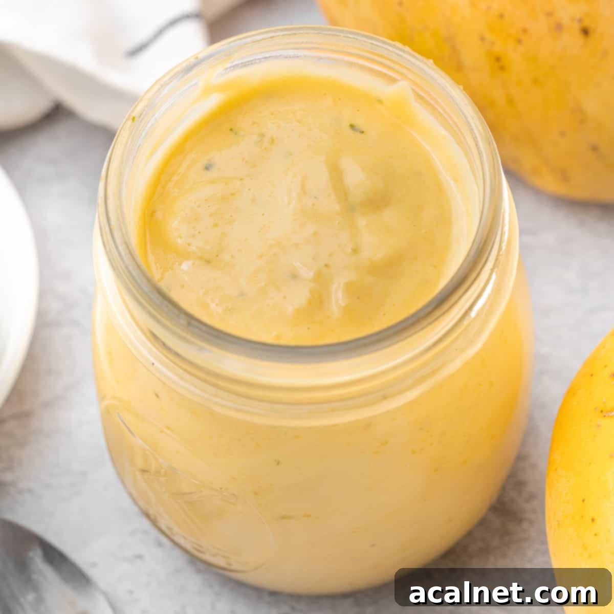Curd seen from above inside a glass jar surrounded by two mangoes.
