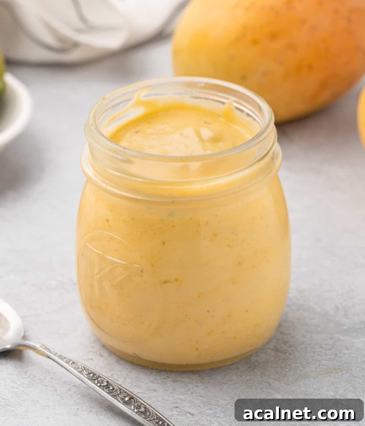 Curd in a glass jar with a mango in the background.