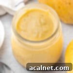 Curd seen from above inside a glass jar surrounded by two mangoes.