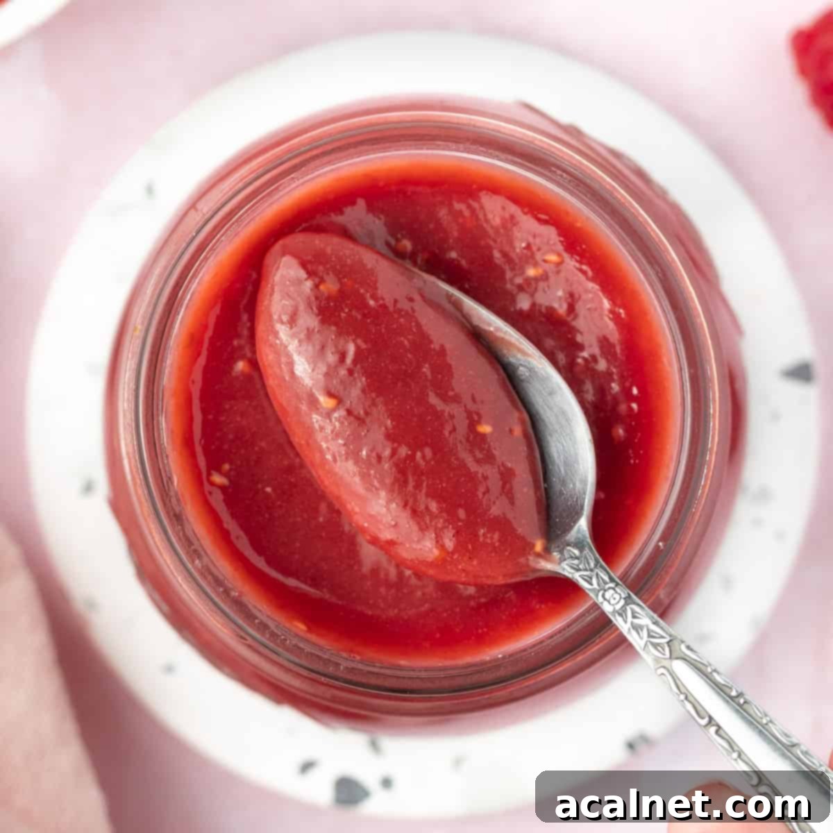 Picking up some raspberry curd from a jar with a spoon, highlighting its creamy texture.