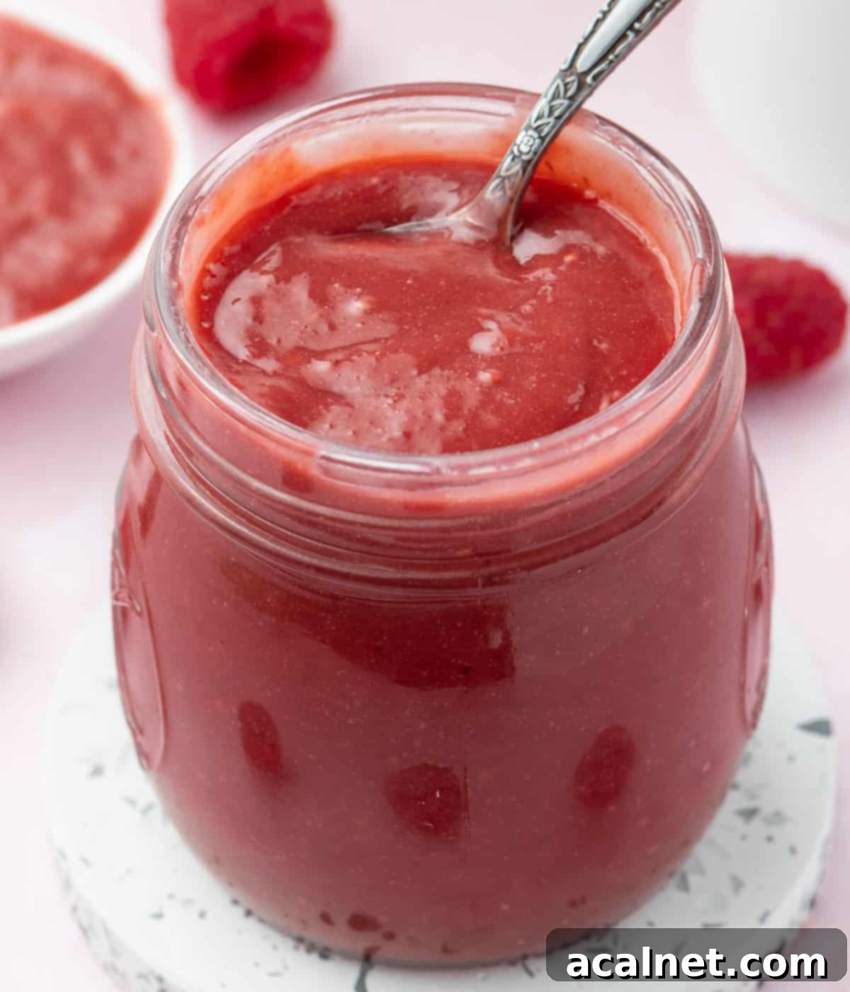Close up shot of creamy raspberry curd in a glass jar with a small spoon, showcasing its smooth texture.