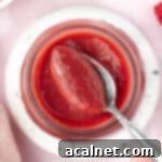 Picking up some raspberry curd from a jar with a spoon seen from above, showcasing its rich color and texture.