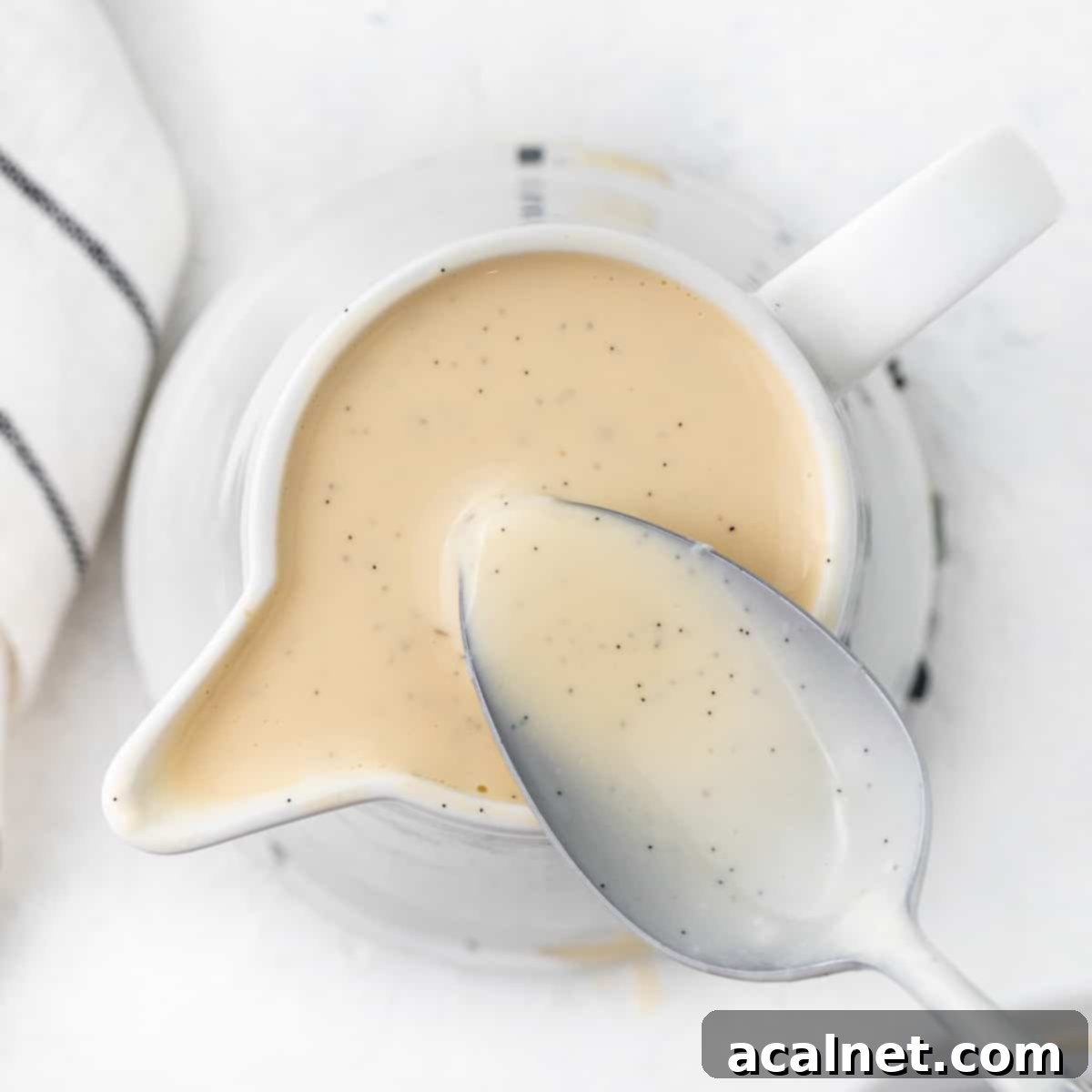 Creme anglaise in a small white jug soon from above with a spoon dipped in.