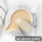 Creme anglaise in a small white jug soon from above with a spoon dipped in.