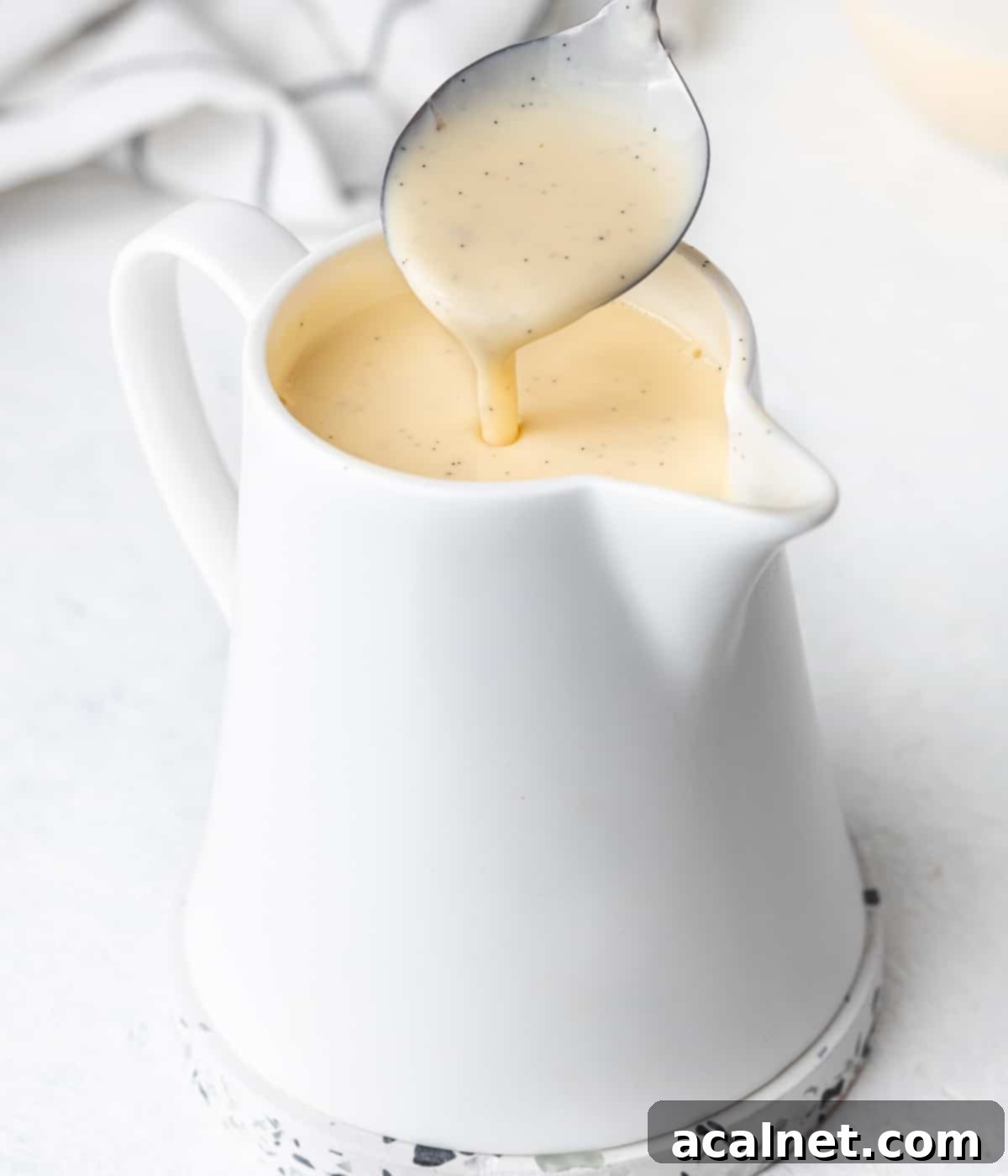 Pouring custard from a spoon into a white jug.