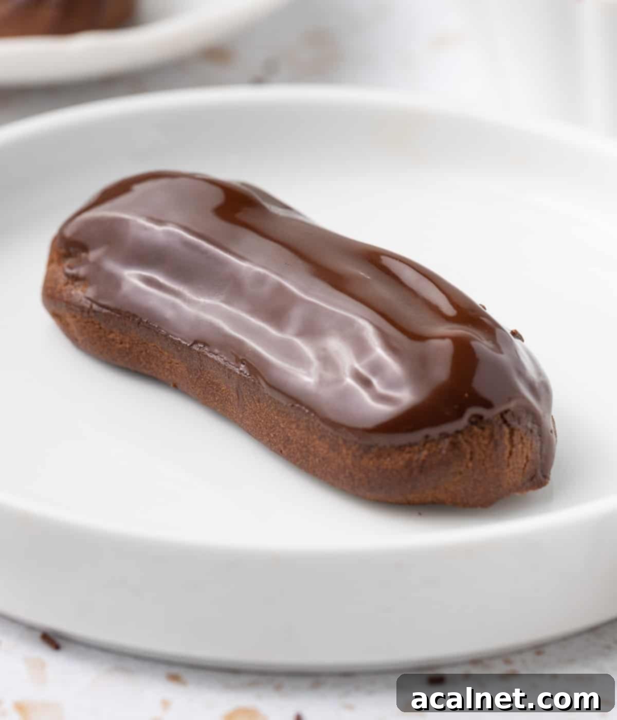 Close up on a glazed eclairs inside a small white shallow bowl.