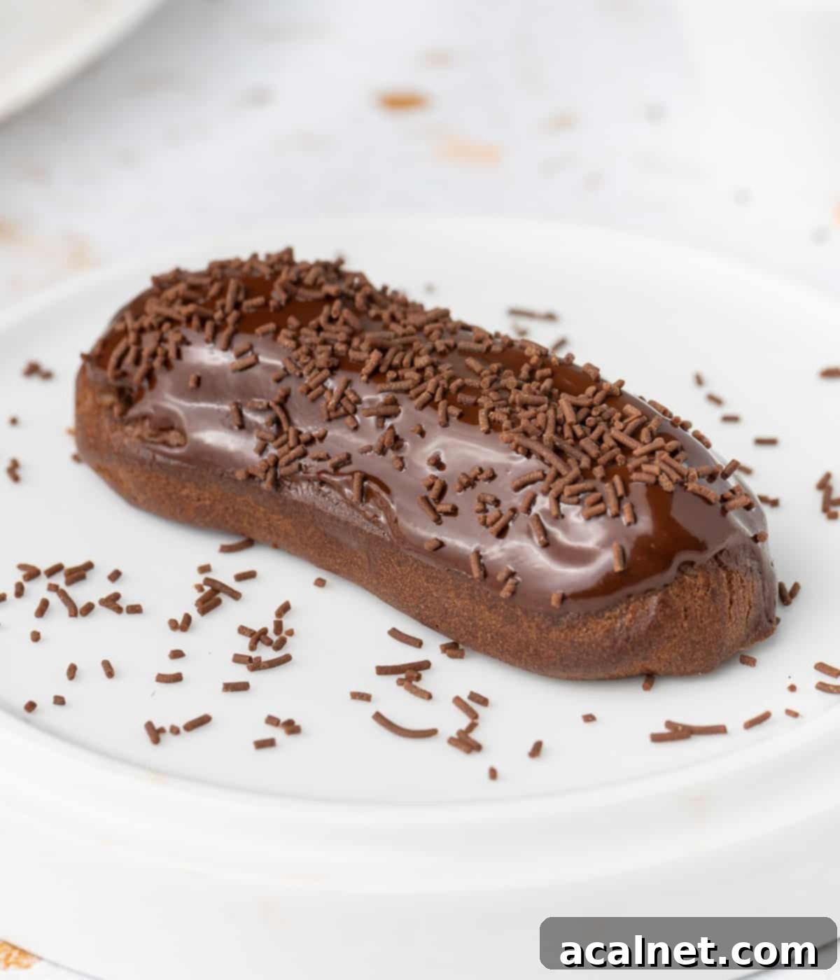 Eclair topped with chocolate sprinkles over a white plate.