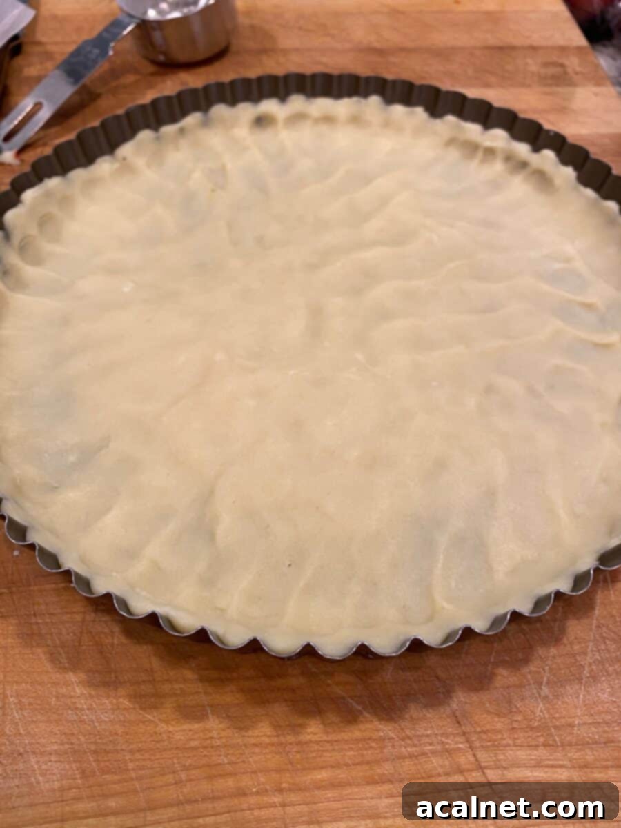 Vibrant Fruit Tart 9 Unbaked shortbread dough evenly patted out to fill the bottom and sides of a tart pan, showing the fluted edge.
