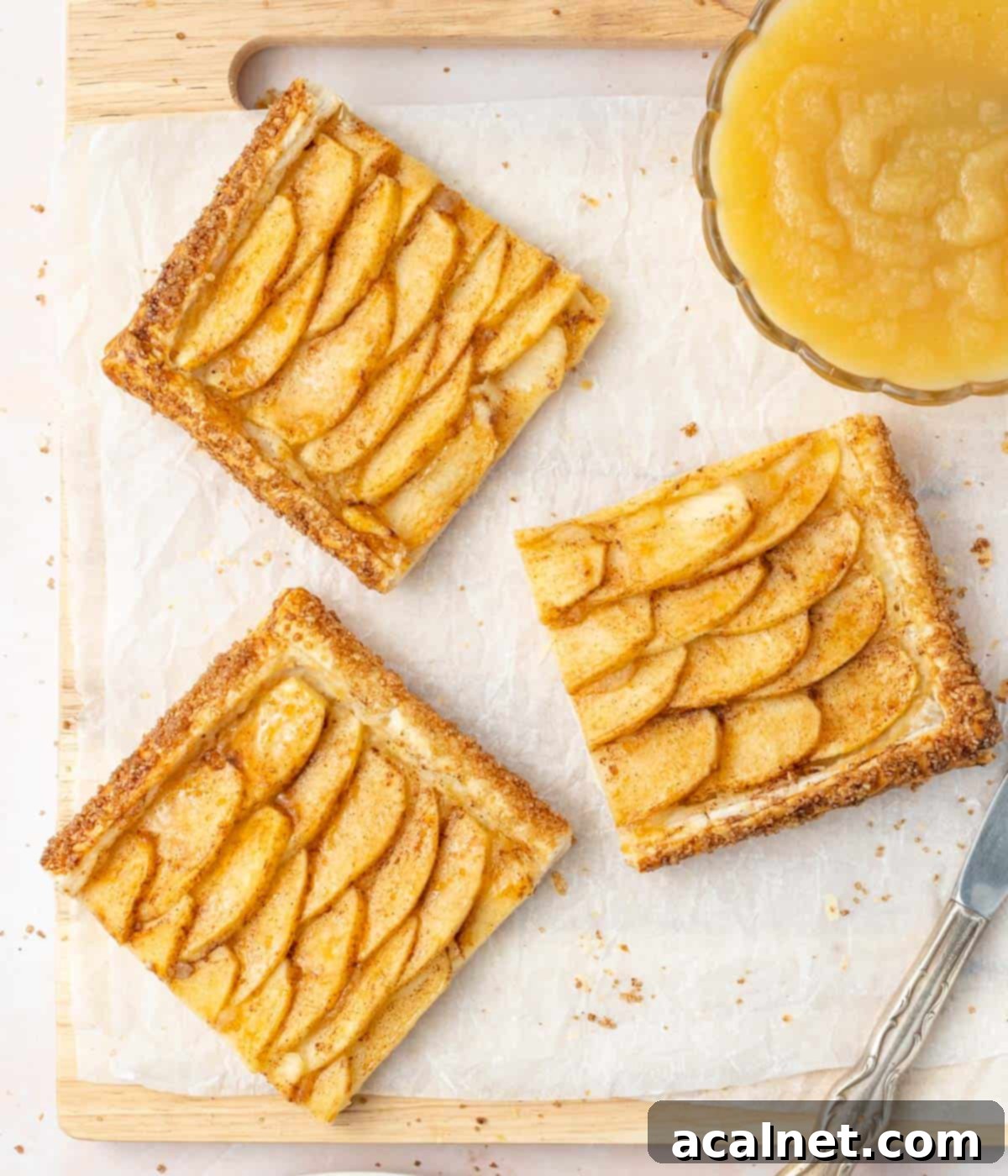 3 slices of tart on a cutting board with a bowl filled with applesauce.