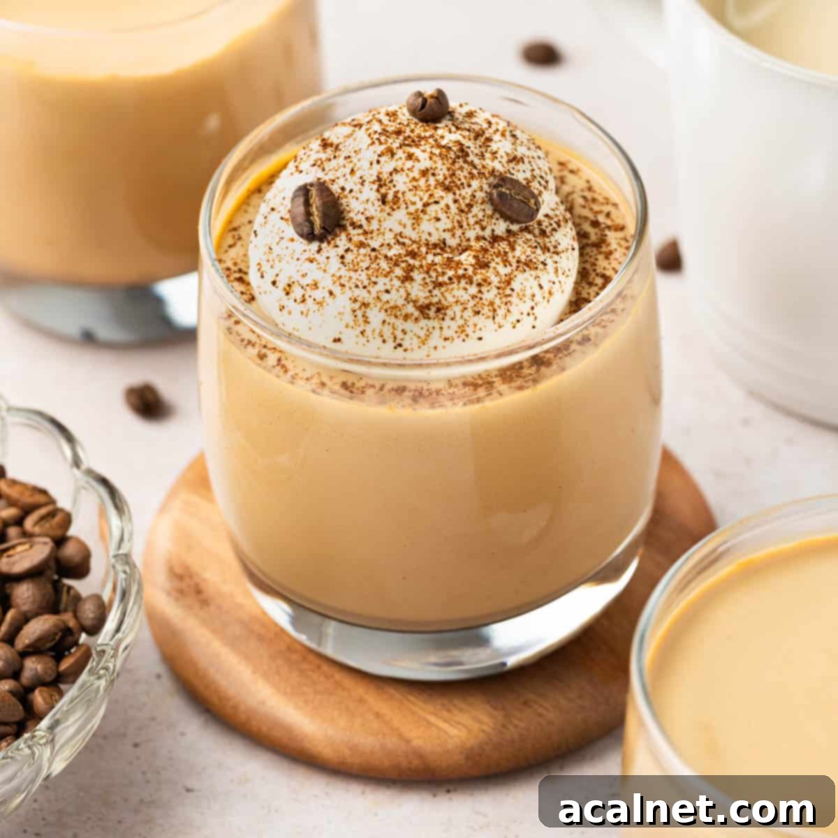 Glass cup of creamy coffee panna cotta, elegantly garnished, resting on a small wooden coaster. The background is softly blurred, highlighting the dessert's inviting texture.