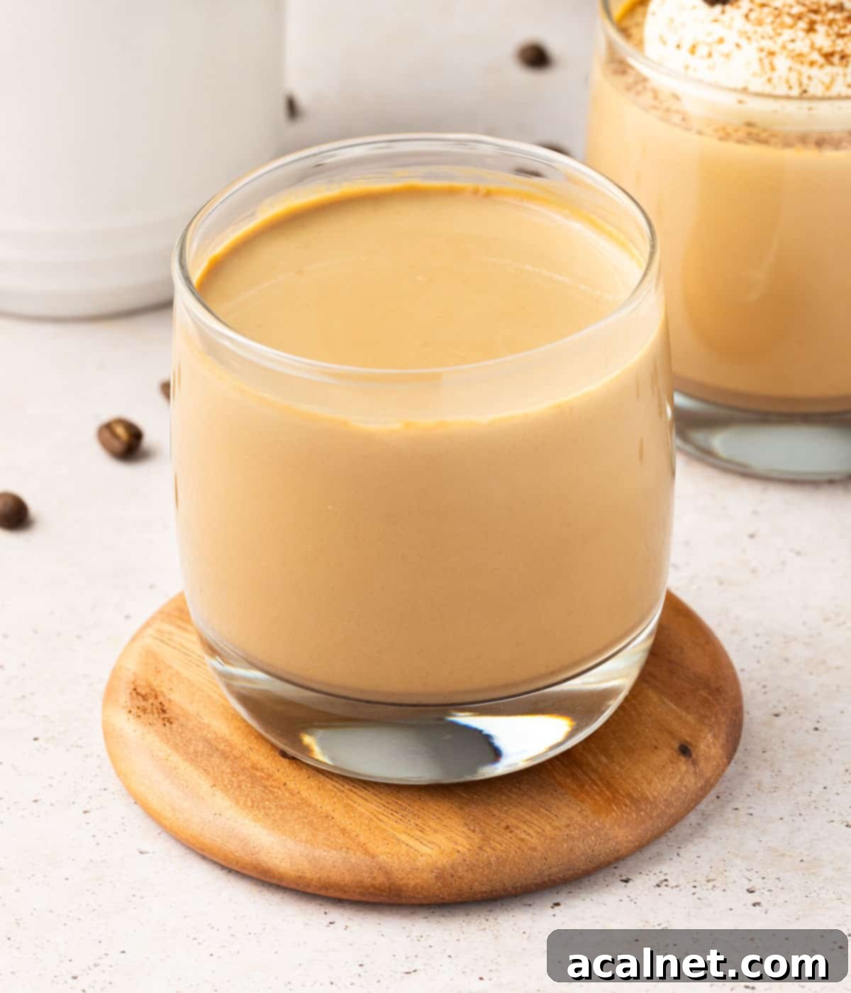 Close-up of a coffee panna cotta mixture being poured into a clear dessert glass, showing its creamy texture.
