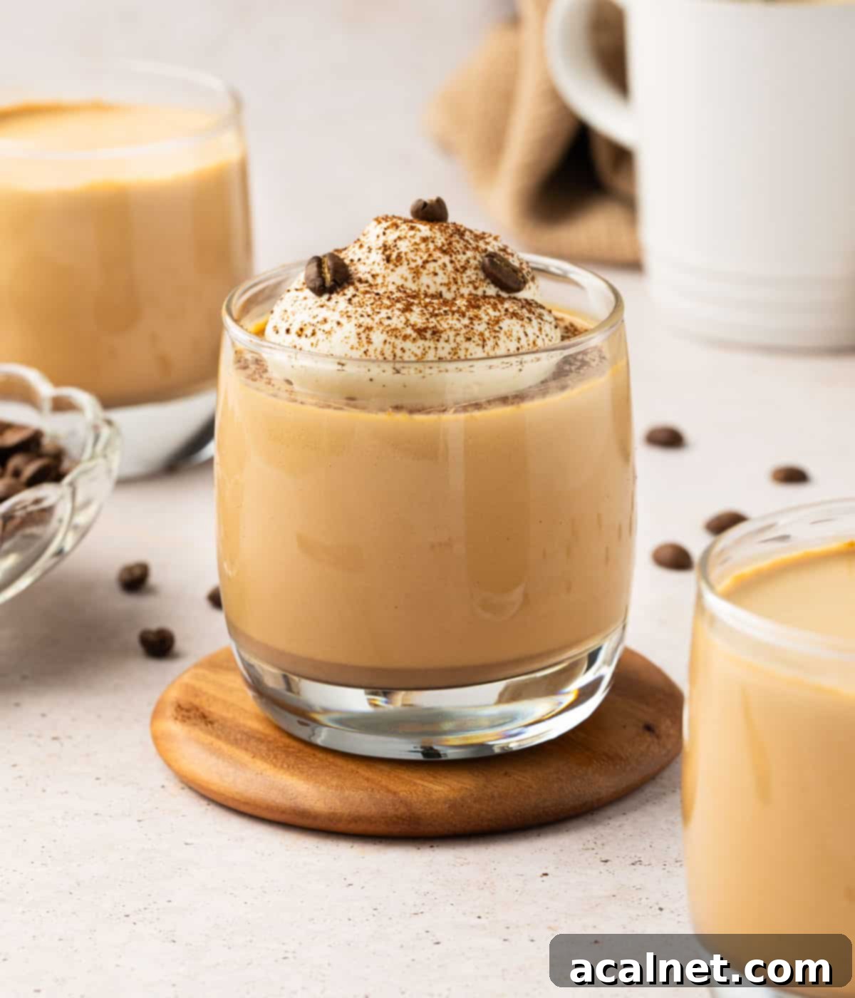 Three perfectly set coffee panna cotta desserts garnished with whipped cream and coffee beans, artfully arranged on a light orange surface with scattered coffee beans around them.