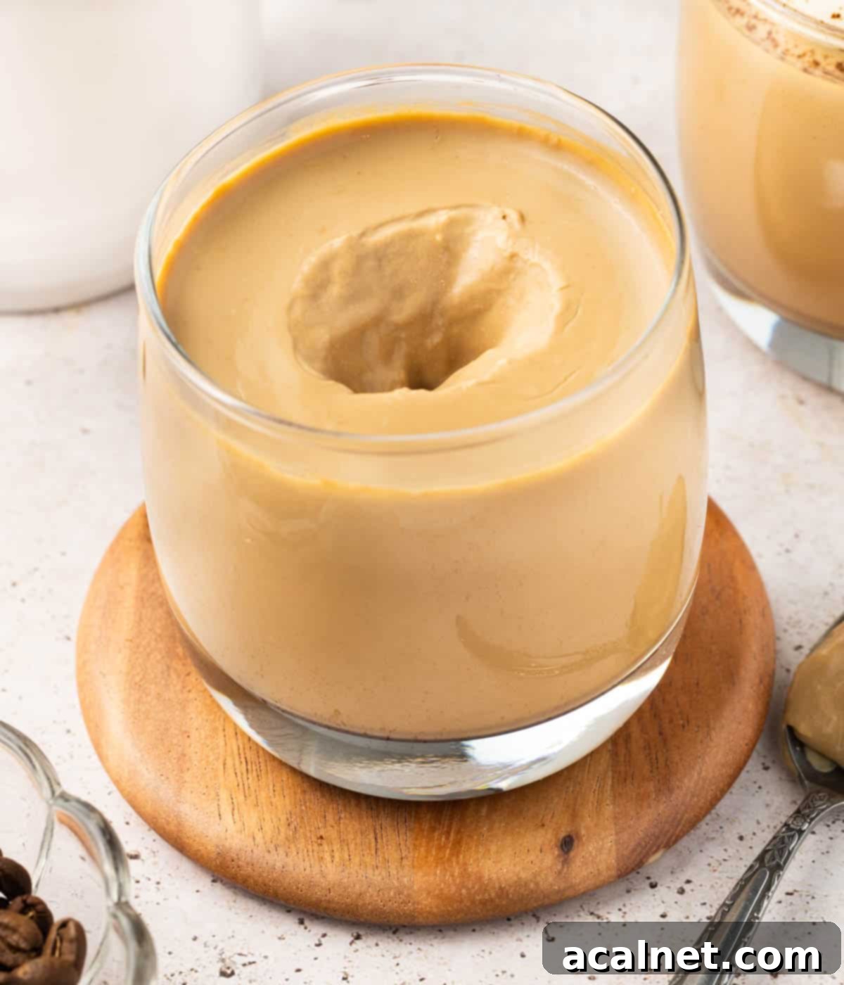 A spoon scooping a portion of creamy coffee panna cotta from a glass cup, highlighting its delicate, wobbly texture.