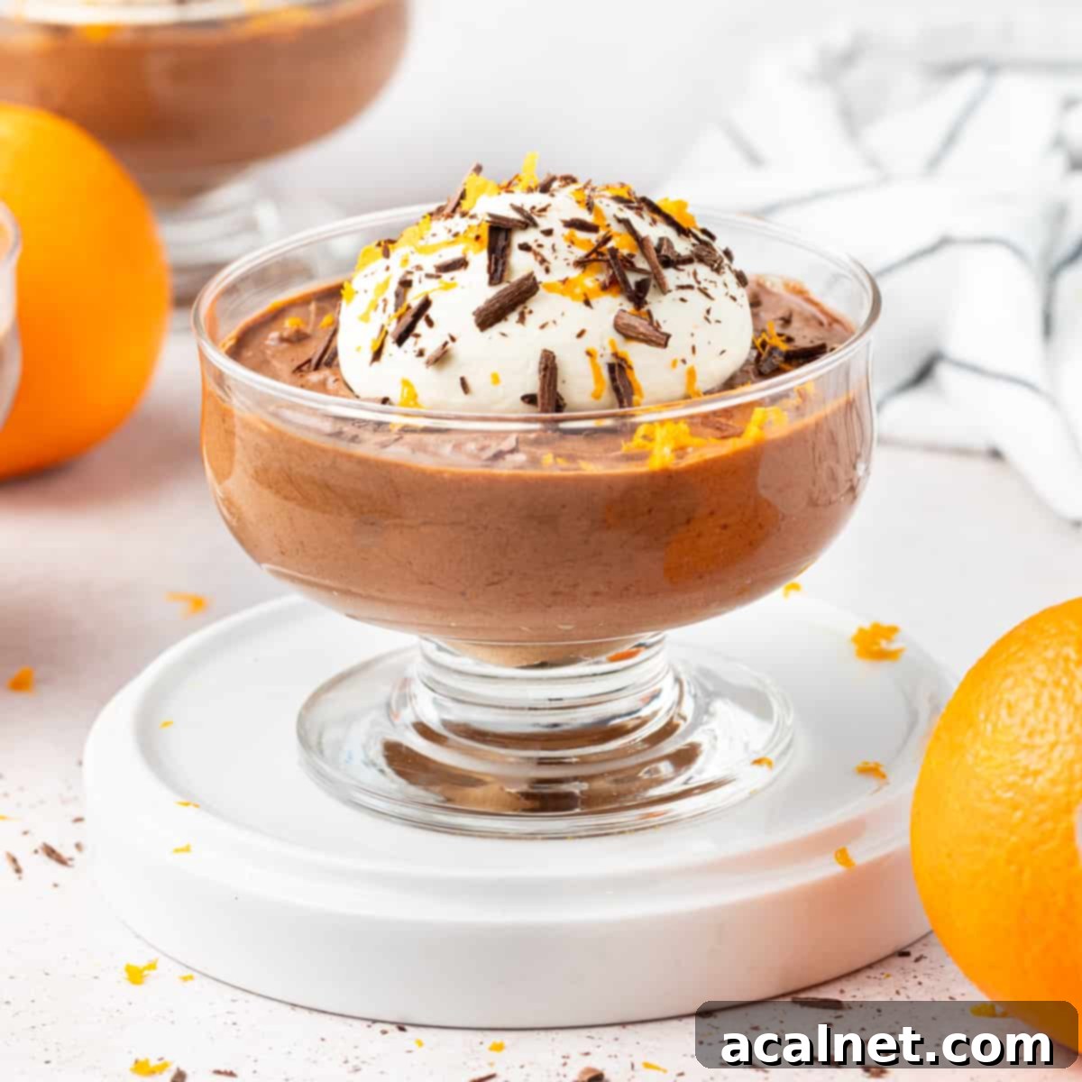 Mousse cup on a white plate surrounded by oranges.