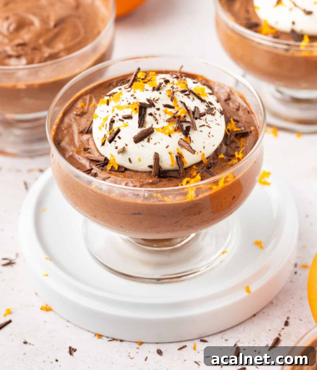 Close up on a mousse topped with whipped cream, chocolate shavings and orange zest.