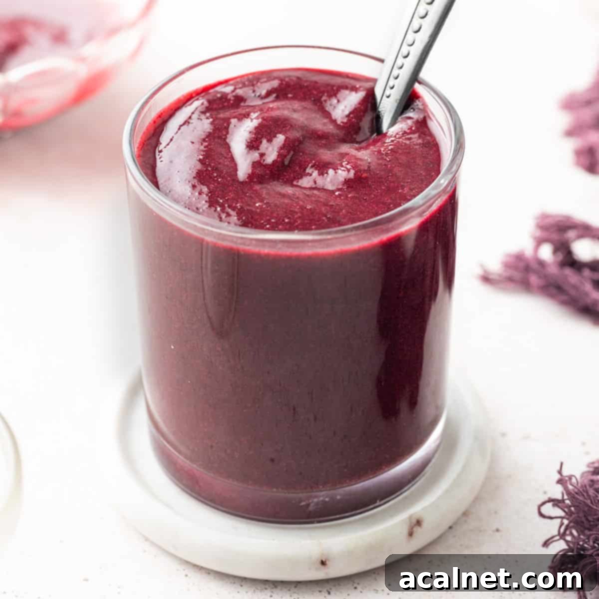 Glass full of berry coulis over a marble coaster with a silver spoon dipped in.