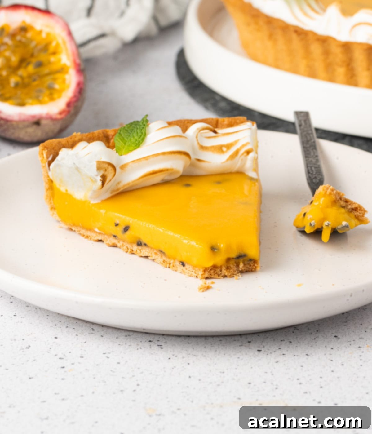 An artfully composed slice of passion fruit tart on a small white plate, with a small portion already enjoyed by a fork, highlighting the delightful texture of the filling and crust.