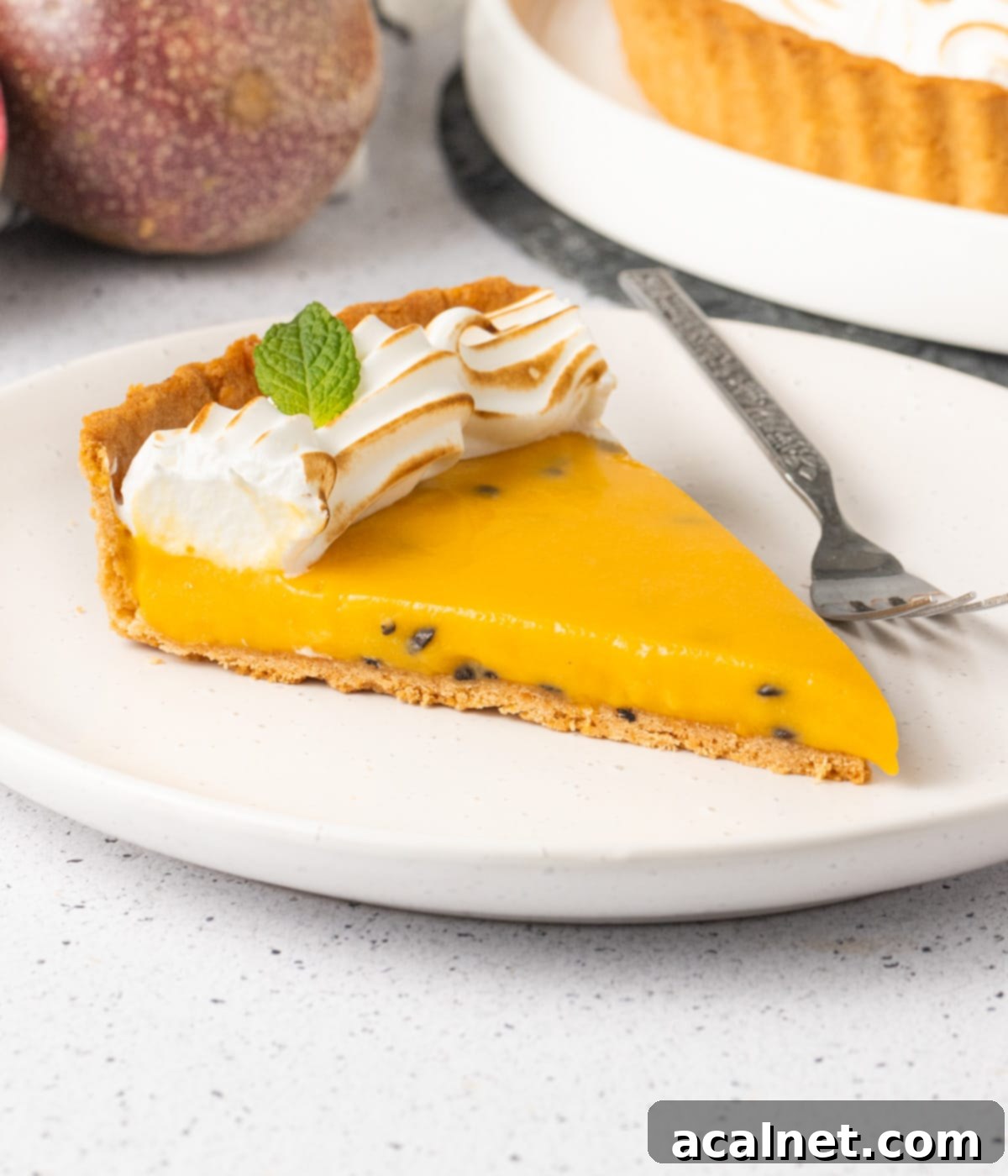A perfectly portioned slice of passion fruit tart presented on a small white plate, invitingly ready to be enjoyed.