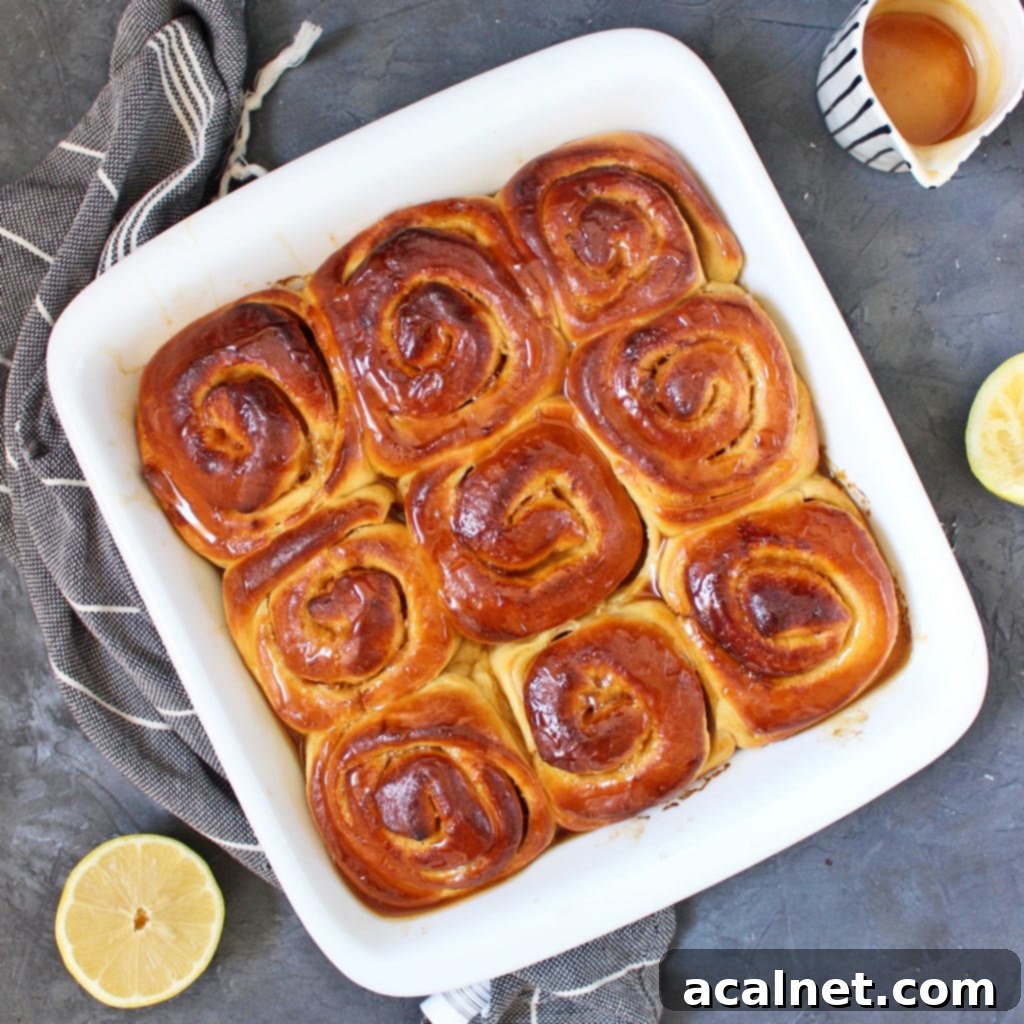 9 fluffy, golden Lemon Sweet Rolls in a white baking dish, drizzled with lemon glaze, viewed from above.