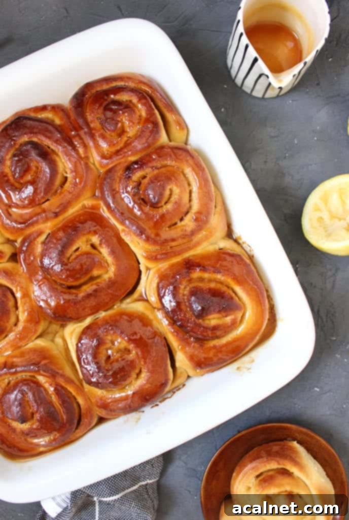 Golden brown Lemon Rolls topped with a glossy lemon drizzle, arranged in a white baking dish, viewed from above.