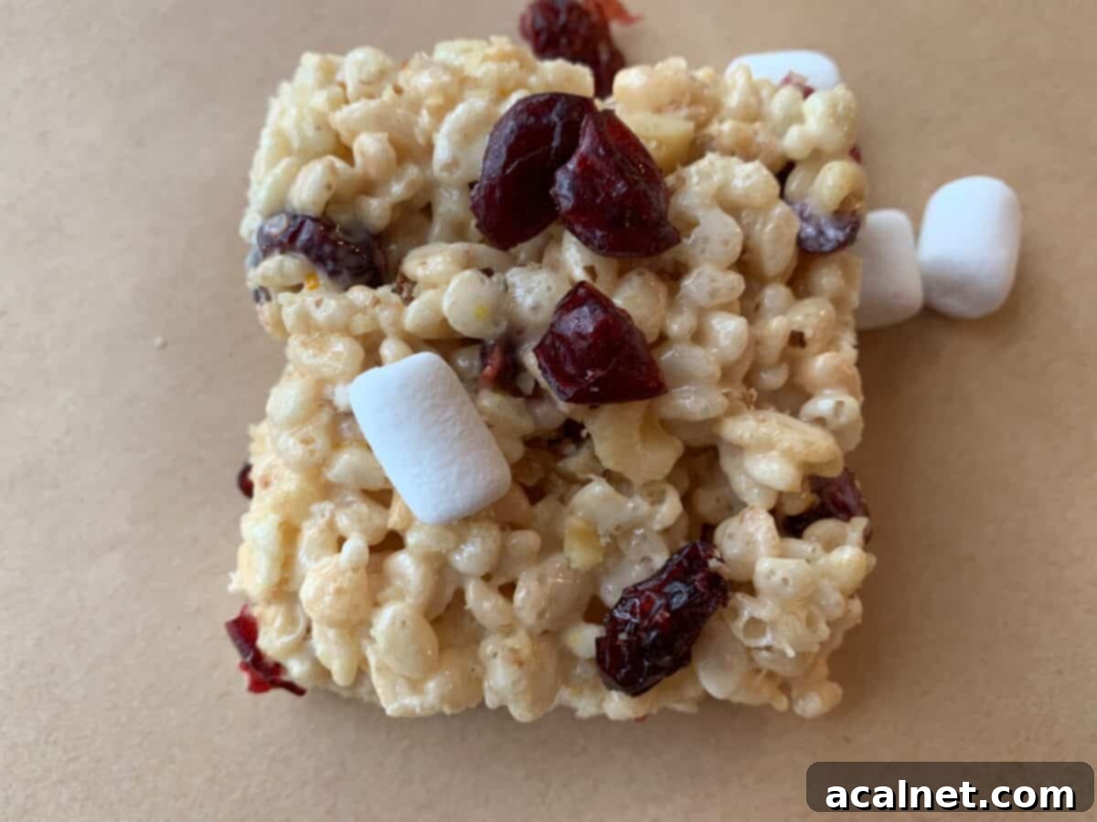 Close-up of a Fancy Rice Krispy Treat square, topped with visible mini-marshmallows, chopped walnuts, and vibrant dried cranberries.