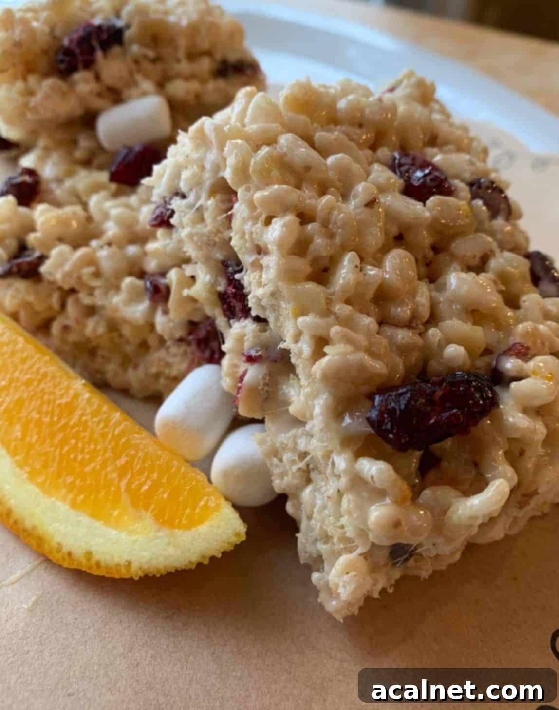 A stack of Fancy Rice Krispy Treats, beautifully arranged with a fresh orange wedge, ready for serving or storage.